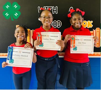 Three girls holding certificates and ribbons.
